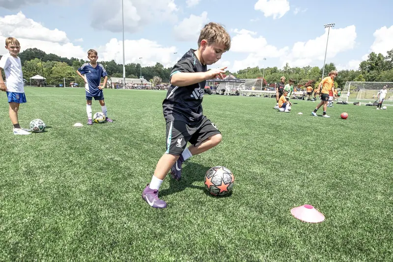 A player in black dribbles between cones on the turf