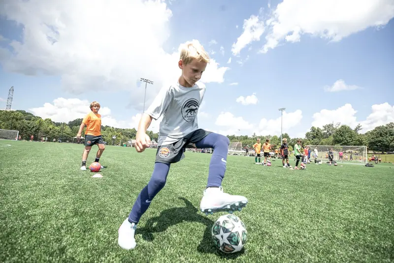 A player in grey takes a first touch under a bright sky